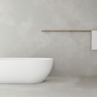 Minimalistisk badeværelse med hvidt badekar for en grå væg med en enkel reol i træ hvor der hænger et hvidt håndklæde