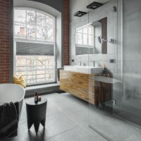 Industrielt badeværelse med rød murstensvæg bagved et hvidt badekar og en brusekabine af glas