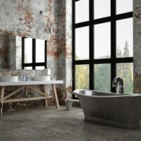 Industrielt badeværelse med stort gulvvindue bagved et rustikt badekar i stål og et aflangt spejl på en murstensvæg