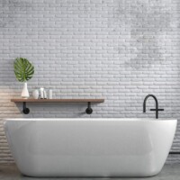 Hvidt badekar foran en hvid murstensvæg og tre sorte rør der går fra gulv til loft