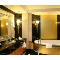 Luksusbadeværelse med et stort spabad med guldklinker foran en stor væg med guldklinker. Ved siden af er der et sort badeværelsesbord foran et stort firkantet spejl