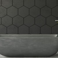 Minimalistisk badeværelse med et stort mørkt badekar foran en grå væg med sekskantede tegl