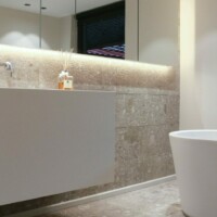 Minimalistisk og lyst badeværelse med et hvidt toilet og et langt aflangt spejl