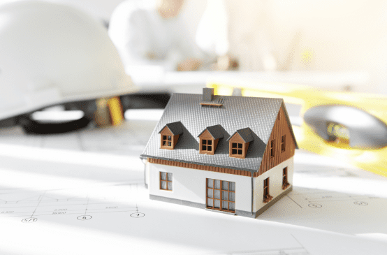 Lille hvid model af et hus på et bord med en hvid arbejdshjelm i baggrunden