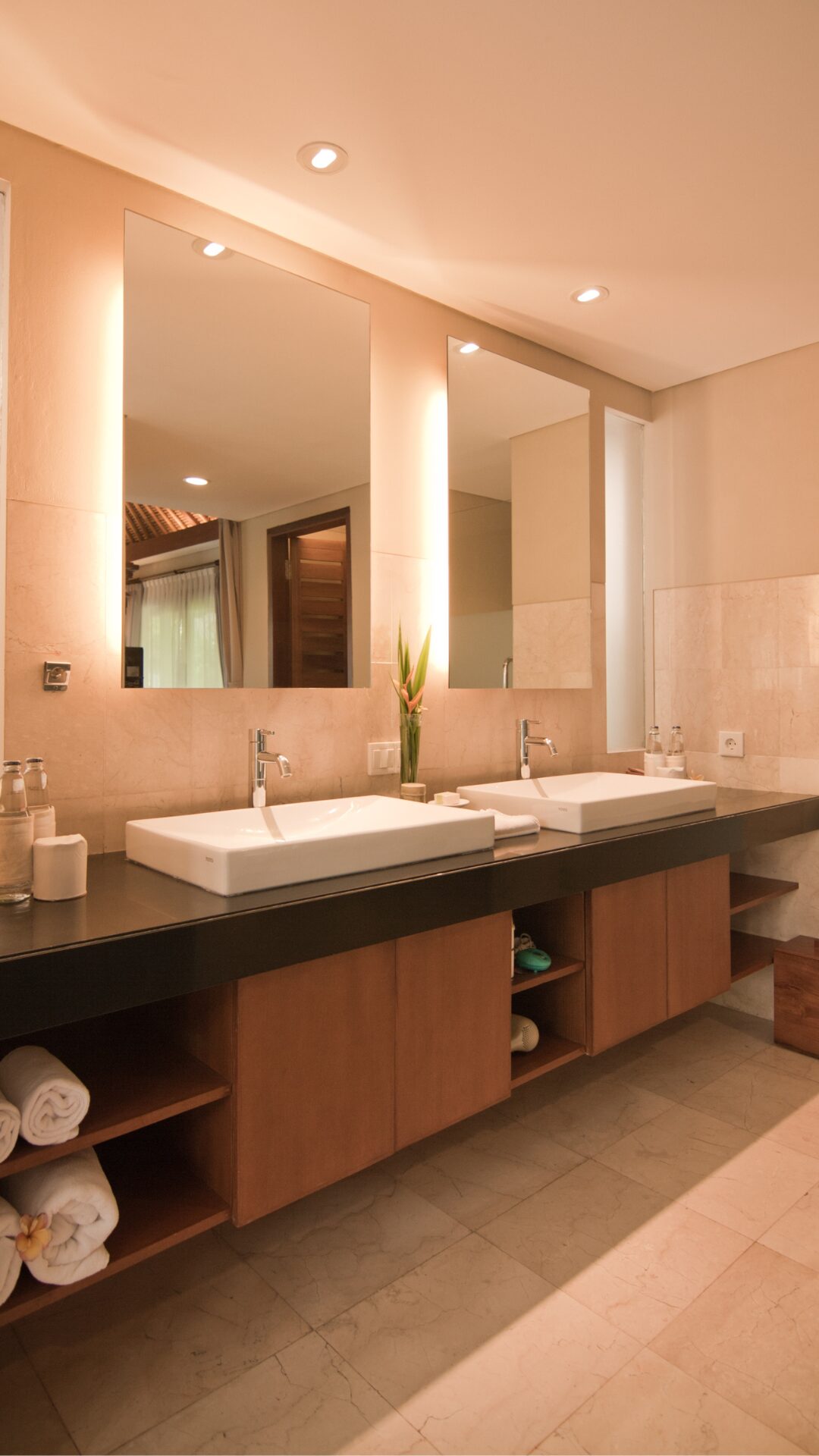 Lyst badeværelse i pastelfarvet lys med to store spejle og to hvide vaske med klinkegulv